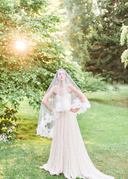bride wearing dramatic chantilyl lace veil with sun shining through trees