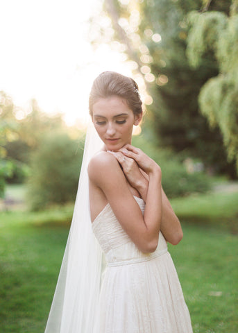 bride looking over shoulder and clasping hands in single layer tulle veil and lace dress